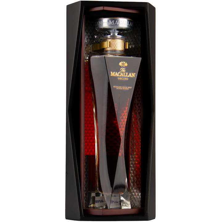 A bottle of The Macallan Oscuro Single Malt Scotch Whisky, matured in sherry-seasoned oak casks, is presented in a tall, uniquely shaped glass decanter with gold accents and an elegant black and red display box.