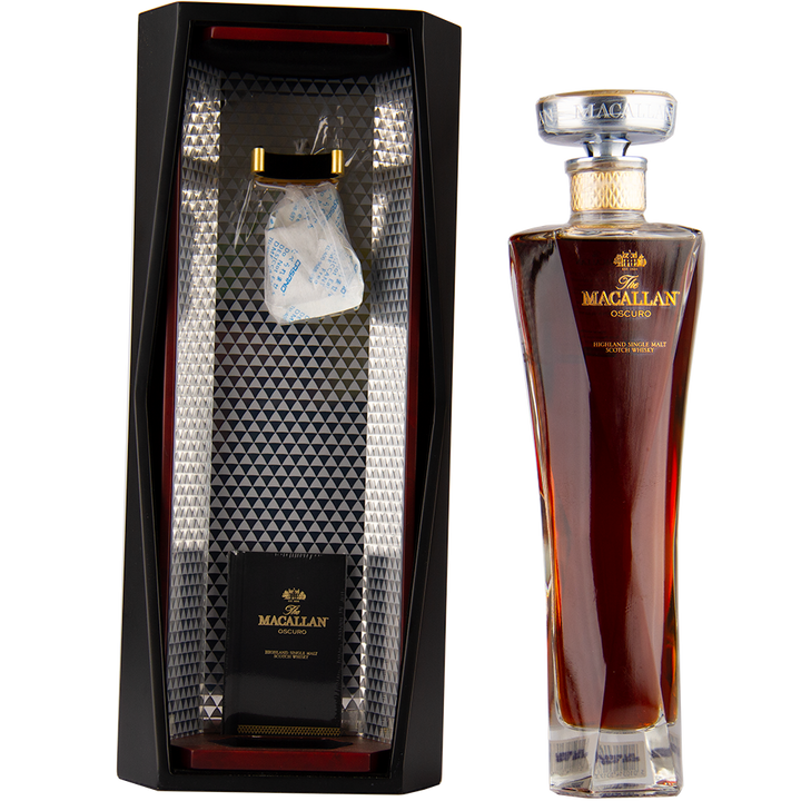 A tall bottle of The Macallan Oscuro Single Malt Scotch Whisky stands beside its geometric black and silver presentation box, open to display the bottle’s slot and a silica gel packet—matured in sherry-seasoned oak casks.