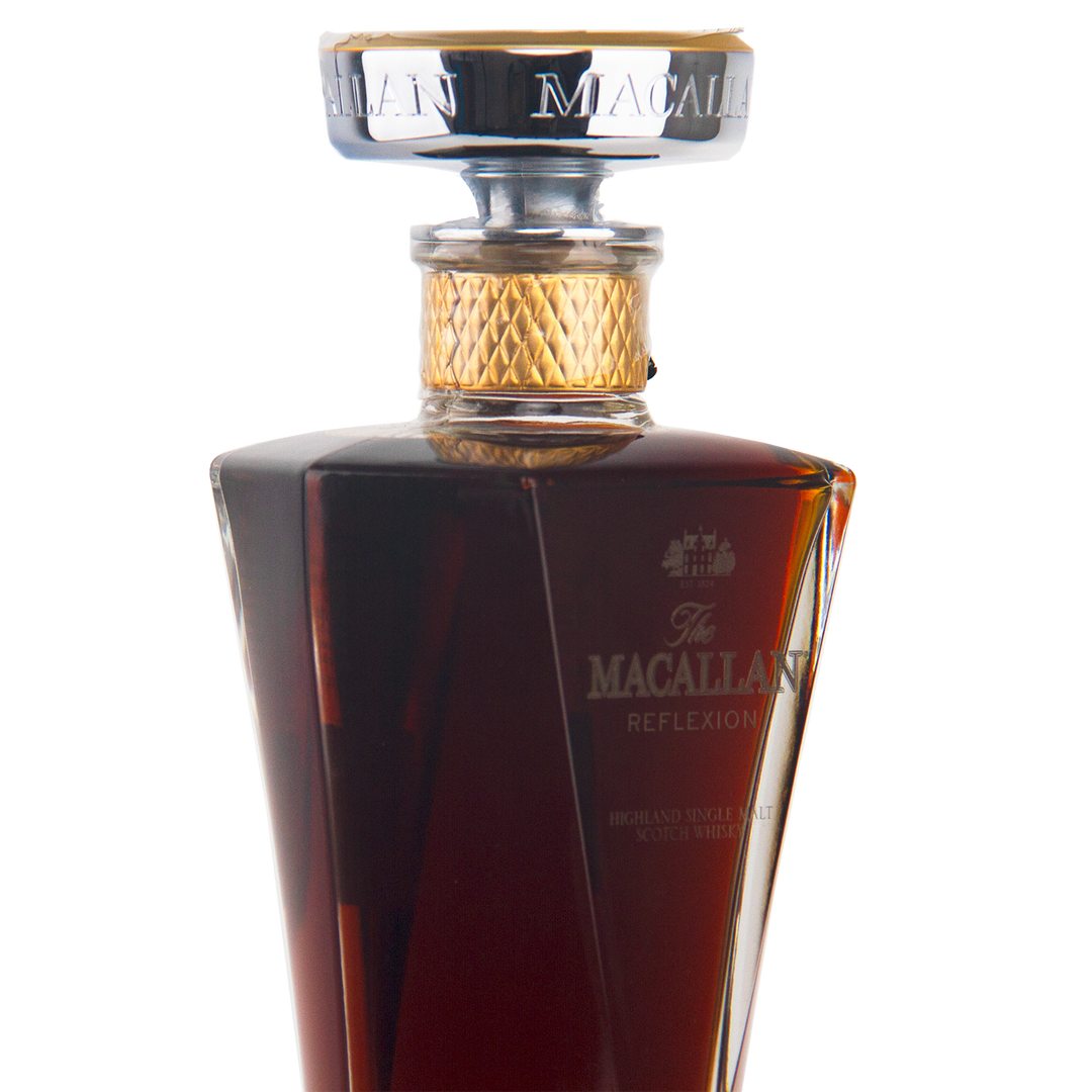 A close-up of The Macallan Reflexion Single Malt Scotch Whisky in a decanter-style glass bottle with a gold and silver cap, showcasing its dark amber hue from sherry cask maturation.