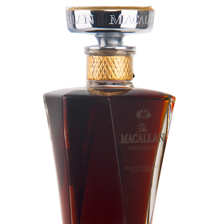 A close-up of The Macallan Reflexion Single Malt Scotch Whisky in a decanter-style glass bottle with a gold and silver cap, showcasing its dark amber hue from sherry cask maturation.