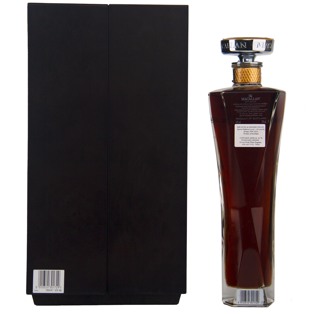 A tall, elegant bottle of The Macallan Reflexion Single Malt Scotch Whisky with dark liquid and a decorative cap stands beside a sleek black box. Both have barcode labels, highlighting the whisky’s angled sides and sherry cask maturation.