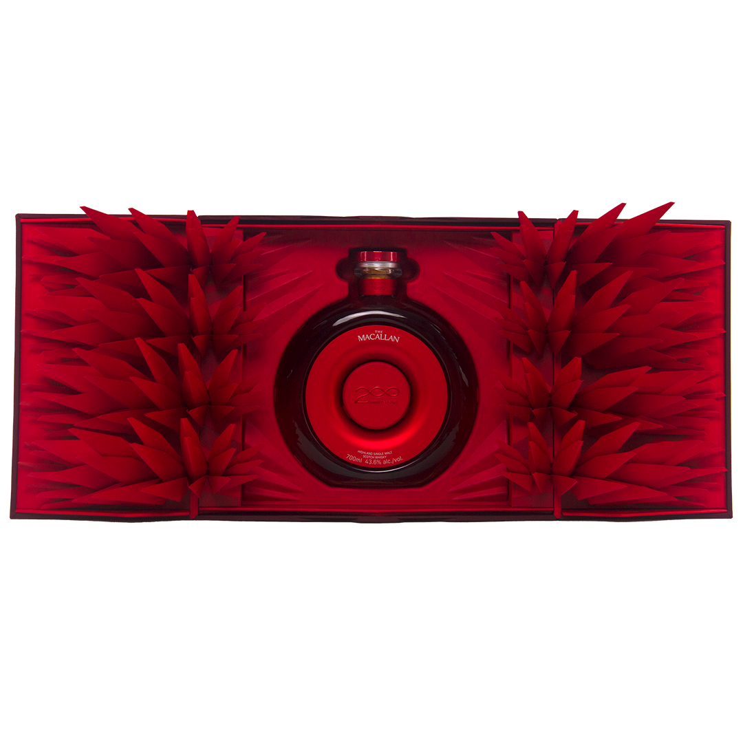 A round red bottle of The Macallan Time Space Mastery Single Malt Scotch Whisky sits at the center of an open, ornate red box adorned with geometric paper spikes, creating a striking and luxurious collectible display.