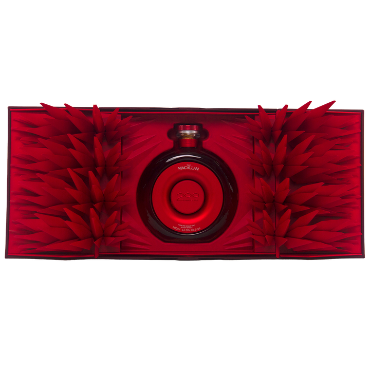 A round red bottle of The Macallan Time Space Mastery Single Malt Scotch Whisky sits at the center of an open, ornate red box adorned with geometric paper spikes, creating a striking and luxurious collectible display.
