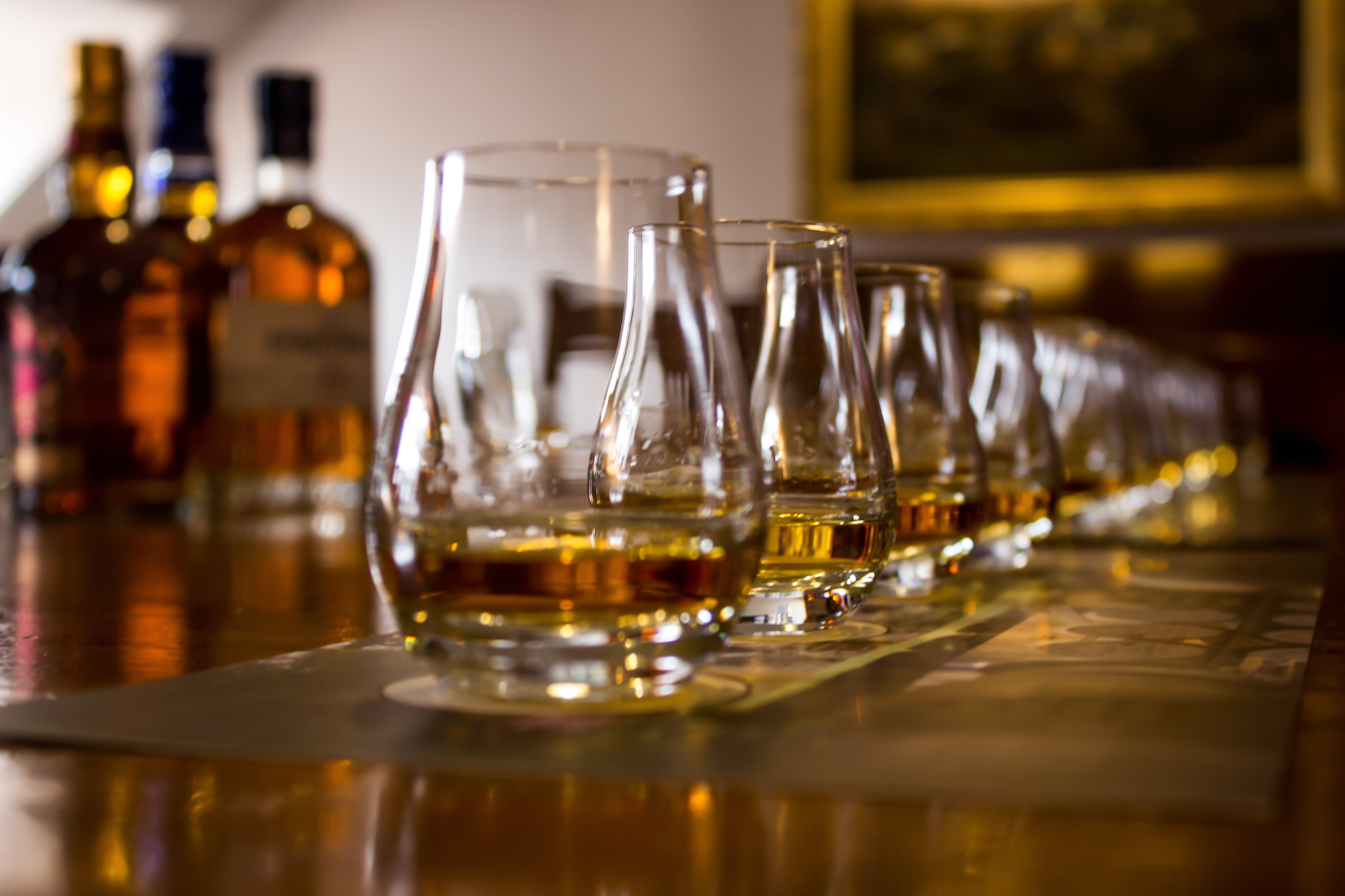 Row of whiskey glasses with bottles in the background