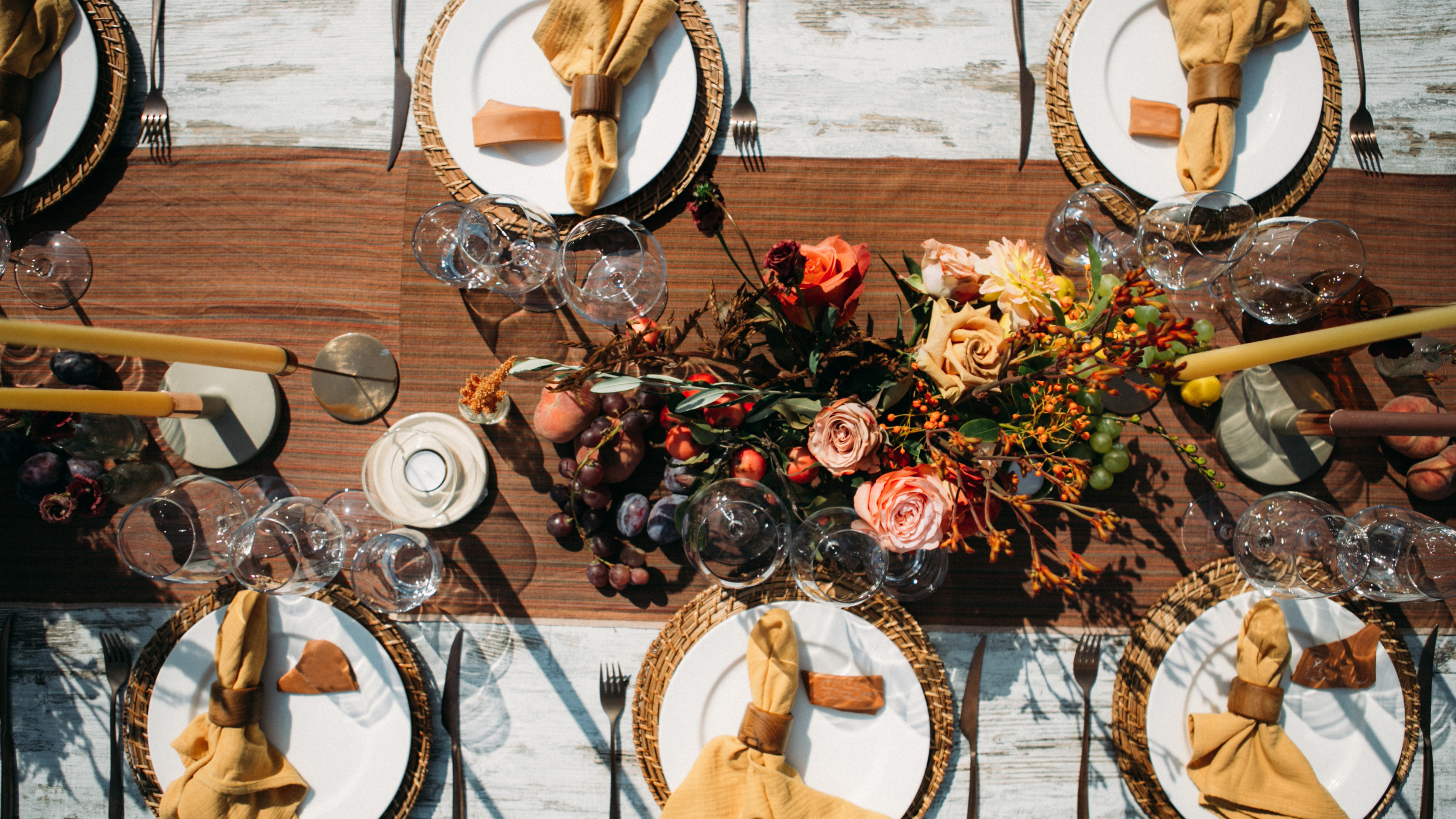 Decorative table setting with floral centerpieces, gold napkins, and white plates on a wooden table.