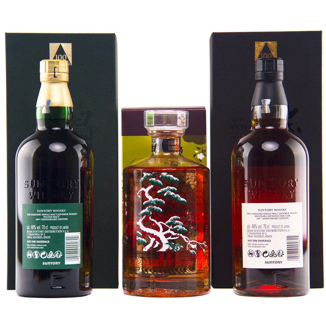 Three bottles from the Yamazaki 18, Hakushu 18, Hibiki 100th Anniversary Set stand before their boxes: green- and black-labeled Suntory whiskies on the sides, and a square Hibiki bottle with an ornate tree design in the center.