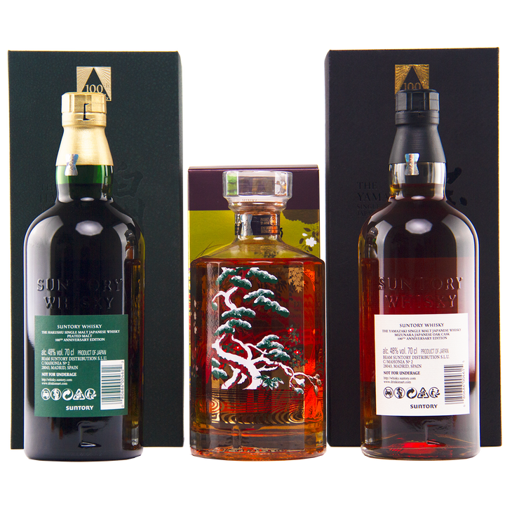 Three bottles from the Yamazaki 18, Hakushu 18, Hibiki 100th Anniversary Set stand before their boxes: green- and black-labeled Suntory whiskies on the sides, and a square Hibiki bottle with an ornate tree design in the center.