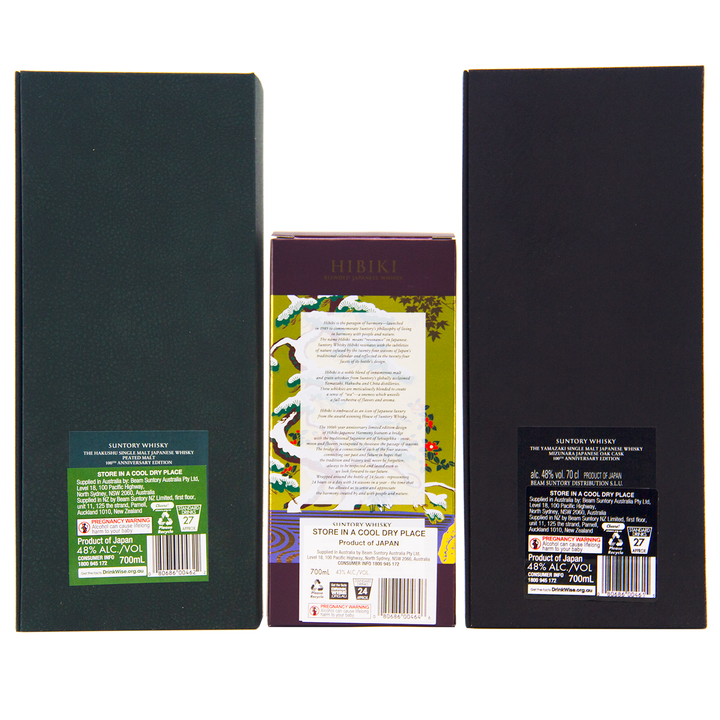 Three boxes—Yamazaki 18, Hakushu 18, and Hibiki 100th Anniversary—stand upright, displaying detailed back labels. The colorful Hibiki box features floral designs, while Yamazaki and Hakushu use elegant dark green and black packaging.