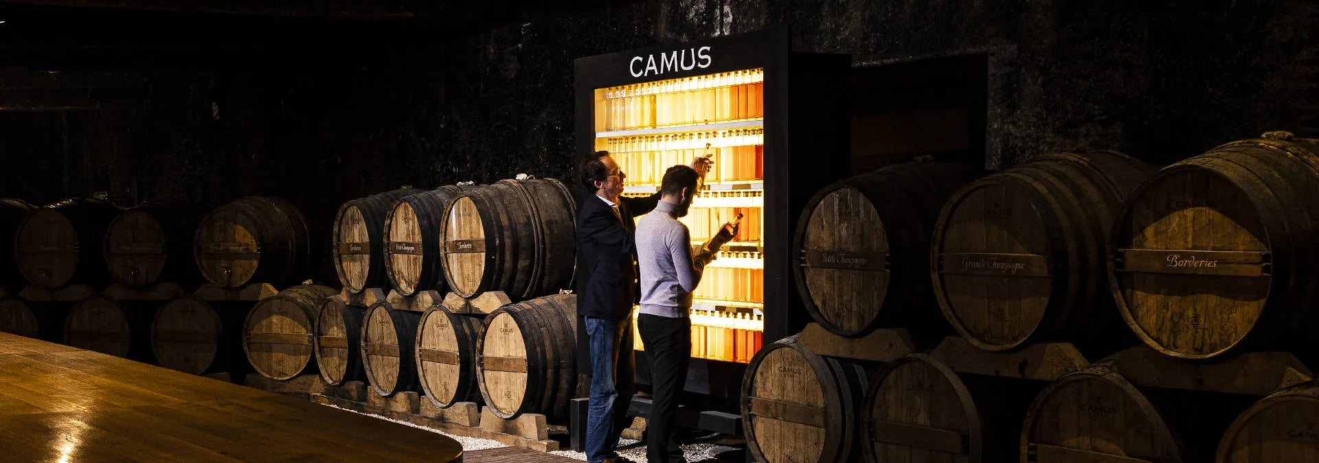 Two people inspecting barrels with a Camus sign in the background
