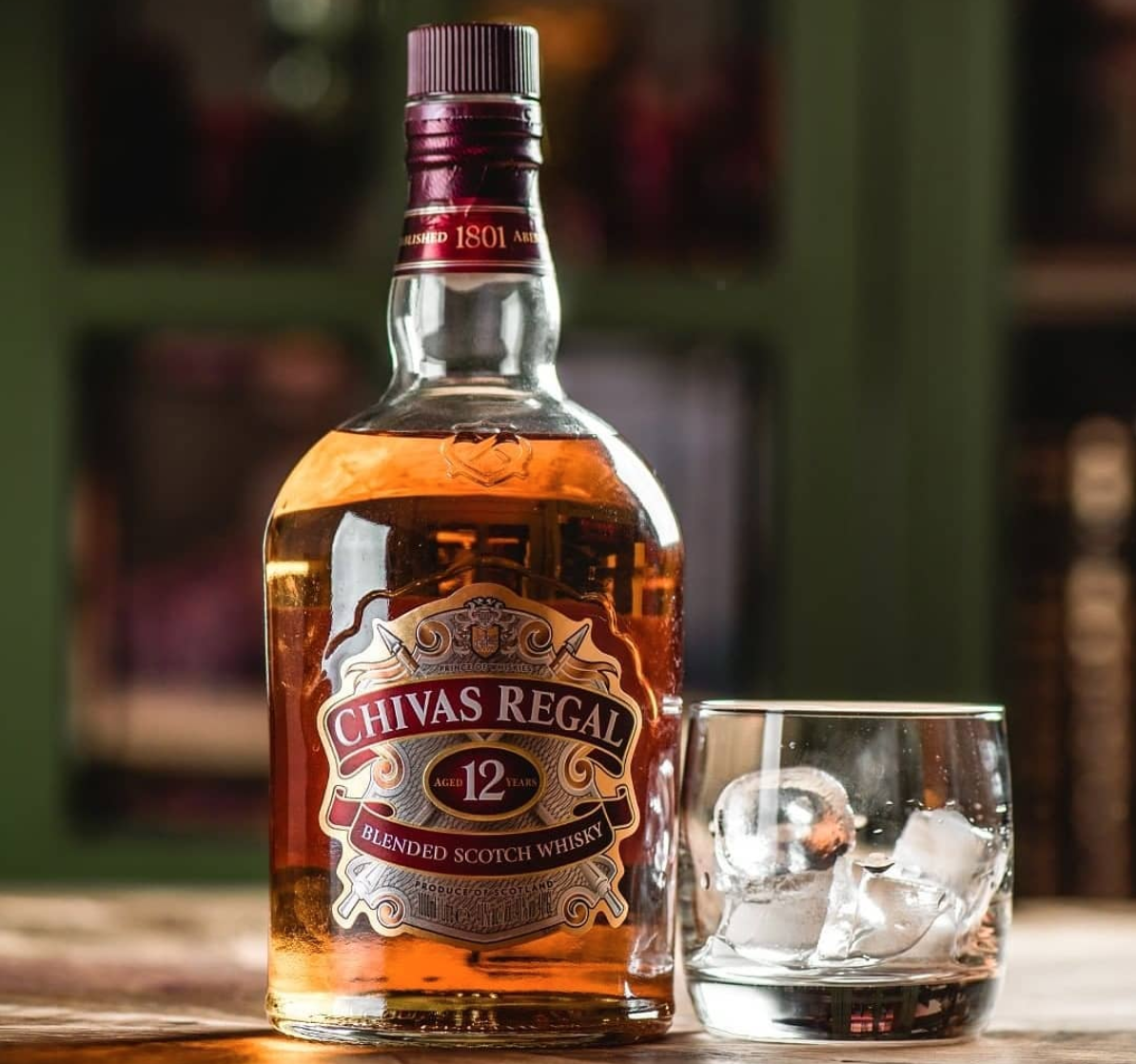 Chivas Regal 12 blended Scotch whisky bottle with a glass on a wooden surface.