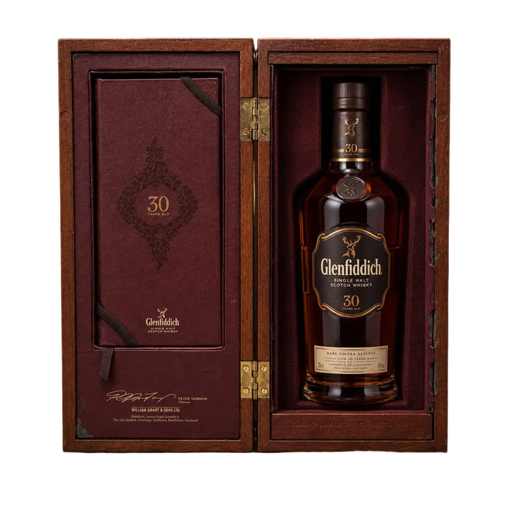 A Glenfiddich 30-year-old single malt Scotch whisky box, opened to show the dark reddish-brown interior packaging, standing on a beige carpeted floor against a white paneled wall.