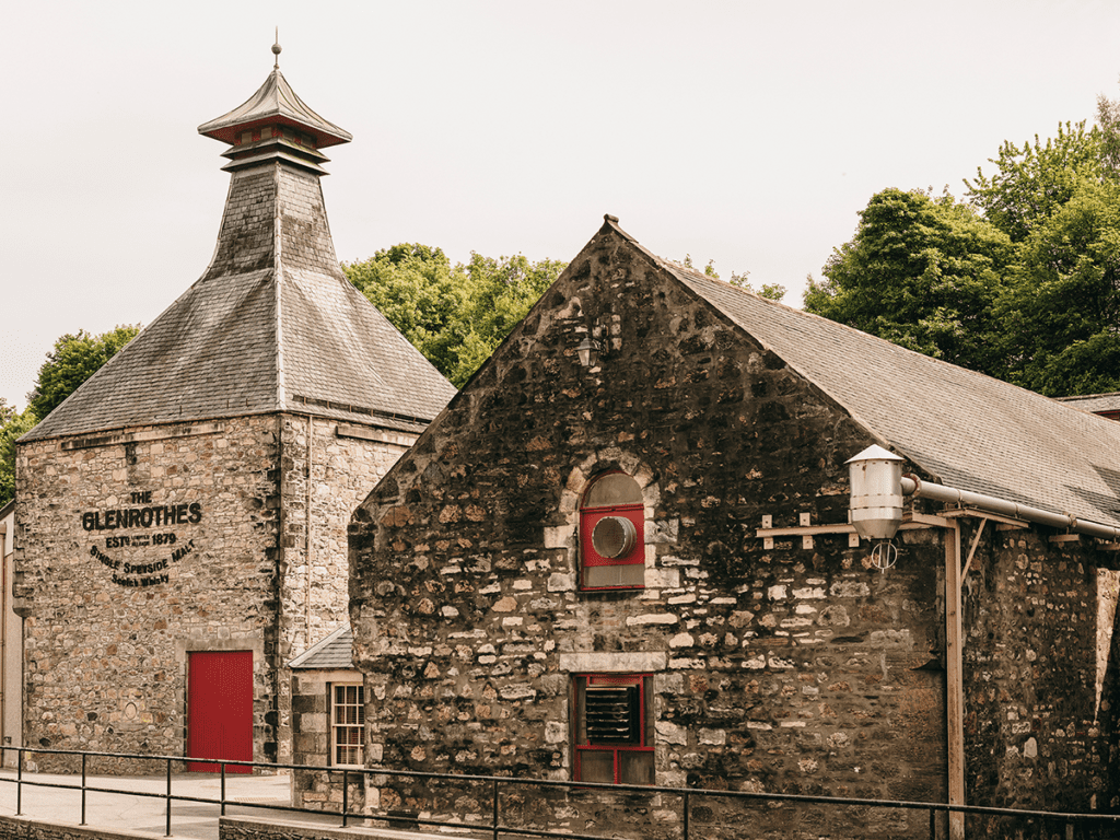 Stone building with a red door and 'The Glenrothes' sign, surrounded by trees.