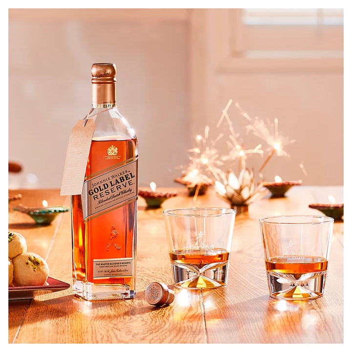 Johnnie Walker Gold Label Reserve bottle with two glasses of whiskey on a table with sparklers in the background.