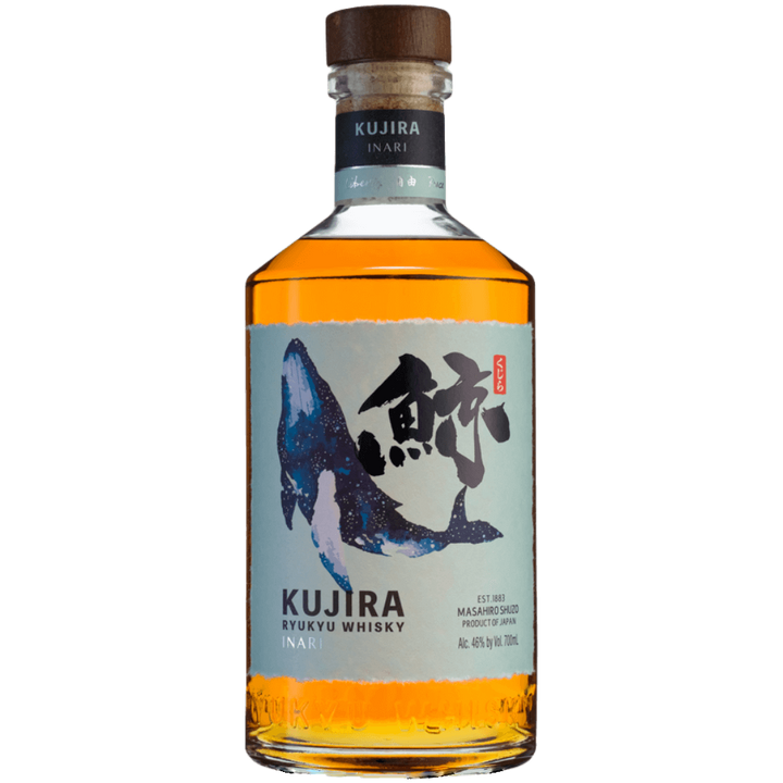 A bottle of Kujira Ryukyu Inari Japanese Whisky with amber liquid, crafted as a Japanese single grain whisky using Okinawan black Koji. It features a blue whale illustration, Japanese calligraphy, a wooden cap, and a blue neck label.