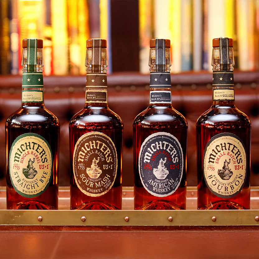 A bottle of Michter’s US*1 American Whiskey stands on a polished bar, highlighting the excellence of unblended Kentucky whiskey amid softly blurred shelves in the background.