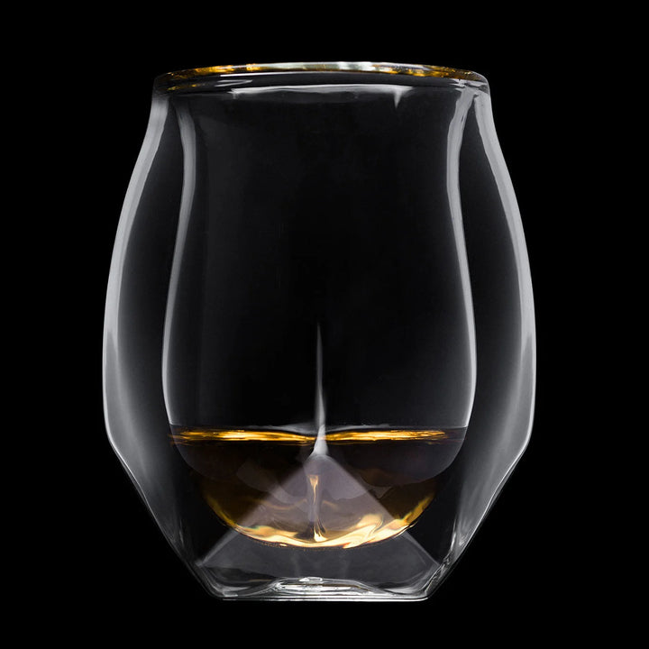 A clear double-walled glass tumbler with a gold rim, shown against a solid black background. The bottom half of the inner glass is filled with amber-colored liquid, creating a reflective gold base.