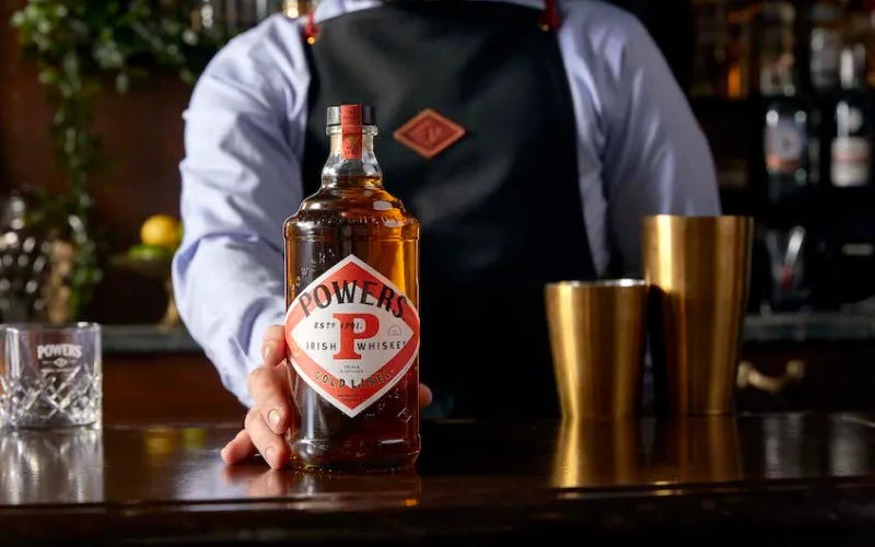 Person holding a bottle of Powers Irish Whiskey in a bar setting