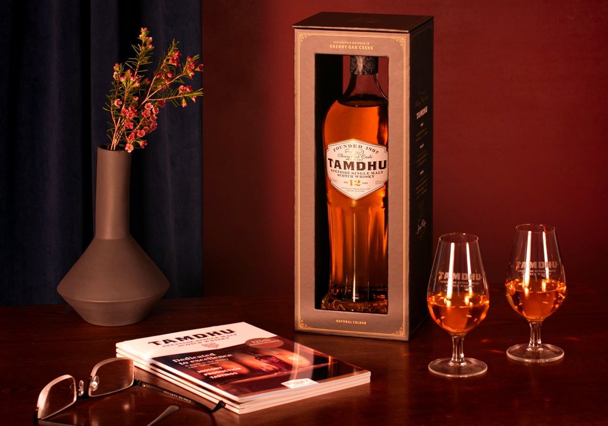 Tamdhu whisky bottle in a box with two glasses and promotional material on a wooden surface.