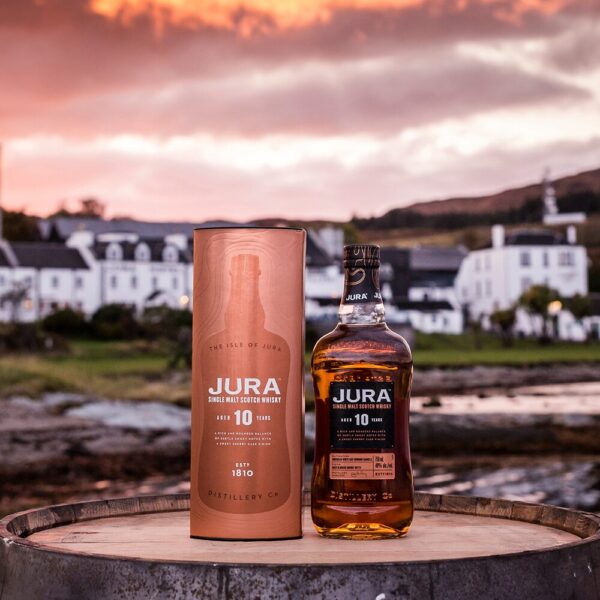 A gorgeous Scottish landscape sets the scene of a bottle of the Jura 10 Year Old single malt whisky with a pink sunset.