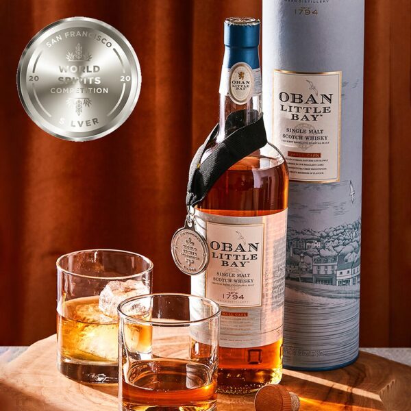 a bottle of the Oban Single Malt whisky Little Bay expression with two glasses of whisky on the rocks.