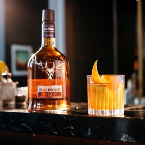 A bottle of the Dalmore 12 year old on a marble bench beside a manhattan cocktail - Whisky Estate