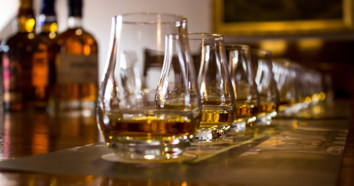 A line of tasting glasses filled with different types of Whiskies for tasting, with the focus on the second glass, the rest is out of focus